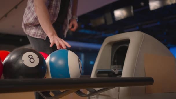Um homem em um clube de bowling pega uma bola de bowling com o número 10 em câmera lenta. Preparação para um lançamento no boliche — Vídeo de Stock