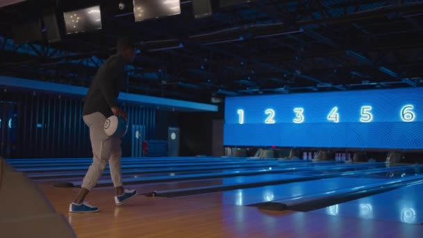 Um homem negro bowling joga uma bola em câmera lenta e derruba skittles. Jogar bowling. Jogue bolas no chão do clube de boliche — Vídeo de Stock