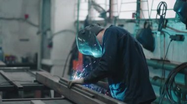 Çalışan bir kaynakçı metal parçalarını gaz veya elektrik kaynaklarıyla yavaş çekimde birbirine bağlar. Çelik ile üretim işi