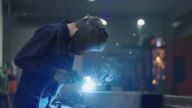 Metal fabrikasında kaynakçılık. Bir kask kaynakçısı kaynak masasına metal bir parça kaynak yapar. Çelik kaynak, kıvılcım, eldiven giymemek, havai fişek gibi açık renkli. Sanayi İşçisi