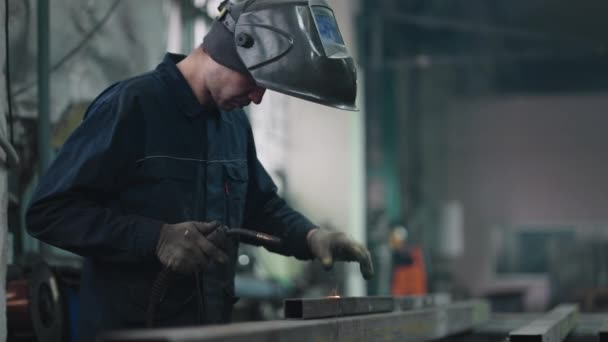 Arbeta i en fabrik. svetsare i speciell mask förbinder metalldelar vid ljusa gnistor — Stockvideo