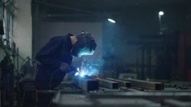 Fabrikada ve dükkanda çalış. Özel maskeli kaynakçı, metal parçaları parlak kıvılcımlarda birbirine bağlar