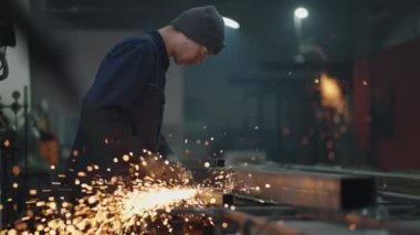 Bir fabrika işçisi kaynak yaptıktan sonra metali öğütüyor. Metal kıvılcımlar saçan üretim odası çalışanı yavaş çekimde uçuyor.
