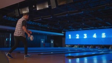 Bowling salonunda bir adam topu ağır çekimde fırlatıyor ve şekerlemeleri deviriyor. Bowling oyna. Bowling kulübünün zeminine top at.