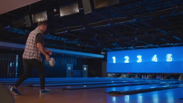 Un uomo in una pista da bowling lancia una palla al rallentatore e abbatte gli skittles. Gioca a bowling. Lancia le palle sul pavimento del bowling club — Video Stock