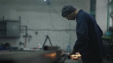 Adam bir fabrikada çalışıyor. Koruyucu gözlüklü bir adam metal cilalama ve çelik metal yapıları sökme ile çalışır..