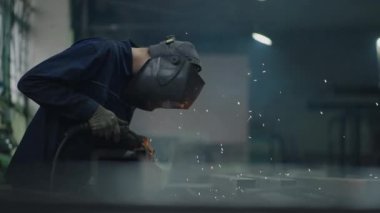 Bir fabrikada kaynakçı olarak çalışan ve çelik metal parçaları ağır çekimde kaynak yapan bir portre. Kıvılcımlar