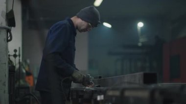 Bir fabrika işçisi ağır çekimde uçan metal kıvılcımlarla çalışır. Koruyucu gözlüklü bir adam metal cilalama ve çelik metal yapıları sökme ile çalışır..