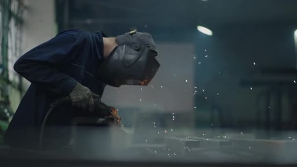 Portrait A man welder works in a factory and welds steel metal parts in slow motion. Sparks fly — Stock Video