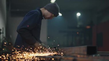 Düşük kamera: Gözlüklü bir adam metal öğütme, parlatma ve çelik metal yapıları sökme ile çalışır.