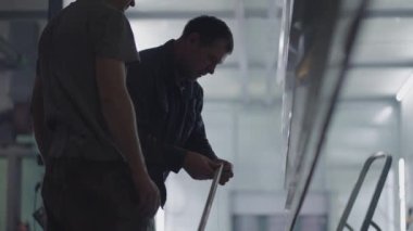 İki erkek ressam, çelik metal elementleri boyamak için onları süspansiyonlarda tamir ederek hazırlıyor. Yapım odasındaki boya parçaları. Ağır çekimde çekim.