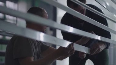 Yakın plan iki erkek ressam çelik metal elementleri boyamak için onları süspansiyonlarda tamir ederek hazırlıyorlar. Boya fabrikası. Ağır çekimde çekim.