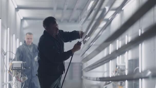Twee mannen aan het werk in de verfwinkel. Molaire werkplaats en werknemer verwerkt stalen profielen van stof en deeltjes alvorens in slow motion te schilderen — Stockvideo