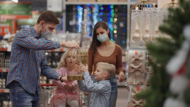 Szczęśliwa rodzina w maskach medycznych w sklepie kupuje świąteczne dekoracje i prezenty w zwolnionym tempie. Cztery osoby ojciec syn córka i matka — Wideo stockowe