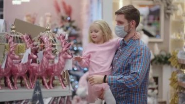 Babası tıbbi maskeli, kızı alışveriş merkezinde Noel için ev dekorasyonunu seçiyor.
