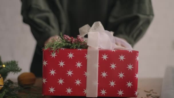 Η κάμερα ακολουθεί το δώρο. Μια γυναίκα με τα χέρια σπρώχνει ένα χριστουγεννιάτικο κουτί με διακοσμήσεις στην κάμερα. Πράσινο χριστουγεννιάτικο δώρο φτιαγμένο με τα χέρια σας από οικολογικά υλικά — Αρχείο Βίντεο