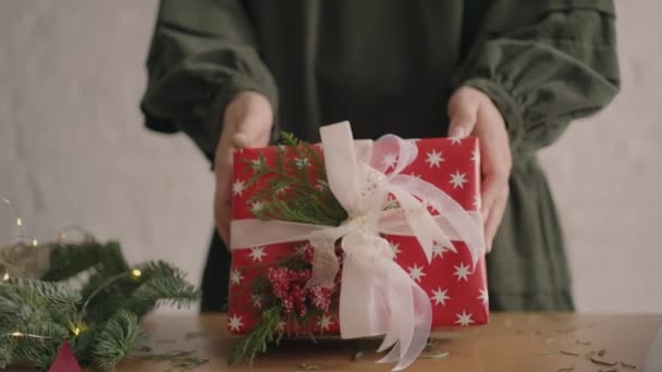 Prezent świąteczny przenosi kobiece ręce do kamery. Czerwone opakowanie prezent kobieta przenosi się do kamery po pakowaniu i dekoracji — Wideo stockowe