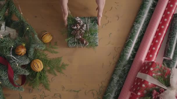 План сверху вниз. Полностью виден стол с украшениями. Рождественский подарок, завернутый в ручную бумагу на деревянном столе. Лента и связанный бант. — стоковое видео