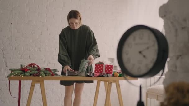Young woman packing Christmas gifts for her friends and relatives, a woman wraps her hands around a box in a Christmas ornament wrapping paper Christmas decorations, preparing for the festive season. — Stock Footage Young woman packing Christmas gifts for her friends and relatives, a woman wraps her hands around a box in a Christmas ornament wrapping paper Christmas decorations, preparing for the festive season. Stock Footage