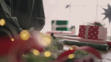 Kırpılmış eller iple paketlenmiş kutuları süslüyor. Tahta masada, Noel kutlaması için hazırlanmış çeşitli dekoratif eşyalarla karton hediye kutusu. İpi bağlayan kadın elleri