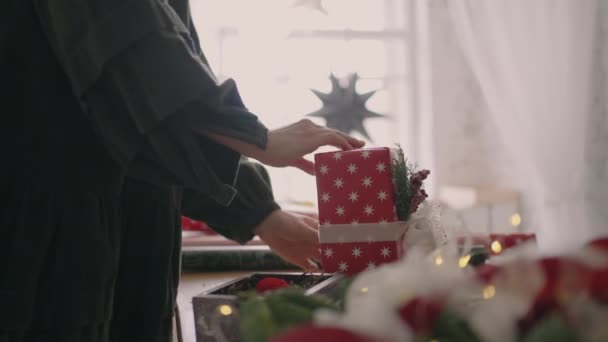Nuori nainen pakkaa joululahjan punaiseen paperiin ja sitoo sen nauhoilla.. — kuvapankkivideo