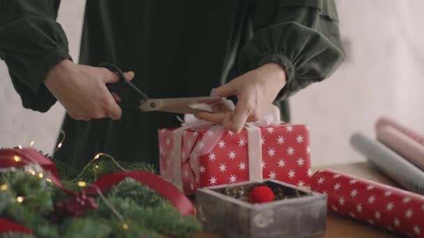 Nahaufnahme einer Dekorateurin mit einer Schere schneidet und schneidet das Band auf der Verpackung eines Geschenks zu Weihnachten — Stockvideo