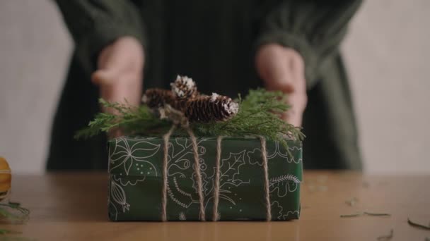 A câmera segue o presente. Uma mulher com as mãos empurra uma caixa de Natal com decorações para a câmera. Bonito presente de Natal feito com suas próprias mãos de materiais eco-friendly — Vídeo de Stock