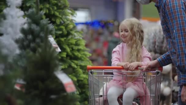Papa und Kind suchen sich Weihnachtsspielzeug im Ladenregal aus. Vater und kleine Tochter im Warenkorb wählen Weihnachtsdekoration. Zeitlupe in Einkaufszentrum — Stockvideo