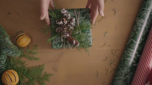 Top view of the decorators desktop Fully visible the table with the decorations. Female hands put and finalize Christmas gift wrapped in craftool paper on a wooden table — Stock Video