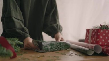 Bir kadının eli, ellerini bir kutuya sarıp bir Noel süsüyle ambalaj kağıdına sarmalar. Profesyonel dekoratör hediye paketi.