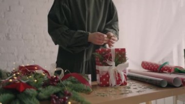 Genç ve güzel bir kadın hediye paketi bir Noel hediyesini paketliyor ve dekoratif çevre dostu dekorasyonlarla süslüyor.