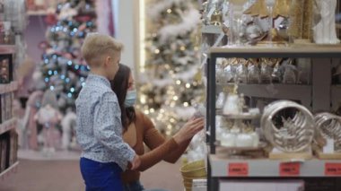 Bir salgında, koronavirüs salgını. Oğluyla birlikte tıbbi maske takan bir anne Noel için ev dekorasyonunu seçer. Noel ağacı oyuncaklarını izle. Coronavirüs salgını