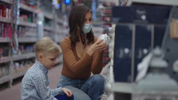 Maskierte Mutter sucht sich vor Weihnachten mit ihrem Sohn Weihnachtsspielzeug aus — Stockvideo