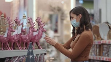 Koruyucu maskeli bir kadın Noel süslerini seçer. Koronavirüs salgınında Noel 'e hazırlanıyorum. Noel ağacı oyuncakları