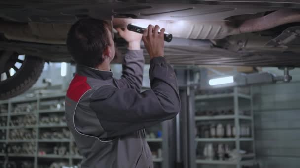 Mekanikern inspekterar bilens avgassystem i biltjänsten — Stockvideo