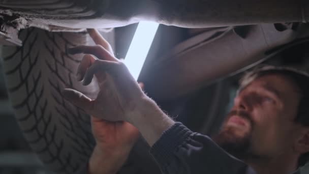 Närbild av handen Mekanikern inspekterar bilens avgassystem i biltjänsten. Bil på hissinspektion och diagnos av problem med upphängning av bilen — Stockvideo