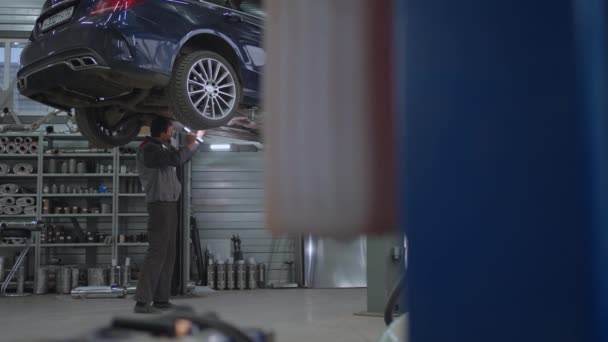 Algemeen Plan De monteur inspecteert het uitlaatsysteem van de auto in de auto service. Auto op de lift inspectie en diagnose van problemen met de schorsing van de auto — Stockvideo