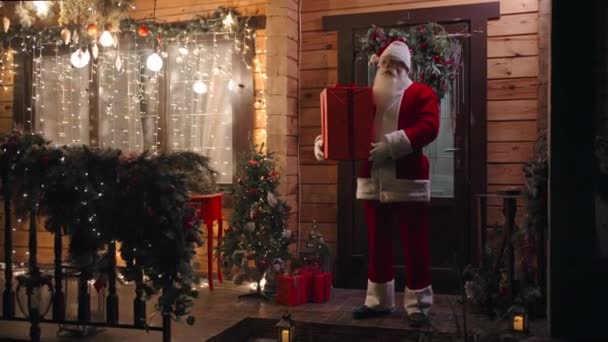 Камера Збільшення Санта Клаус стоїть на вулиці взимку з подарунком і дивиться в камеру. — стокове відео