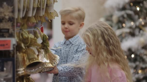 Duas crianças pegando brinquedos de decoração de árvore de Natal para o Natal em uma loja — Vídeo de Stock