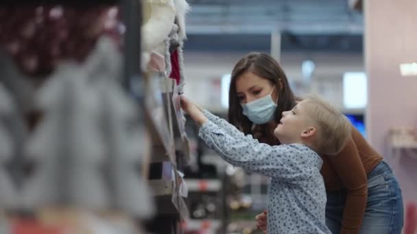 Una mujer y un niño van de compras y eligen árboles de Navidad y juguetes con decoraciones para Navidad en máscaras protectoras — Vídeos de Stock