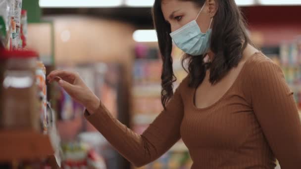 한 여자가 유행하는 동안 보호용 마스크를 쓴 채 슈퍼마켓에서 쇼핑을 하고 식료품을 줍는 모습 — 비디오