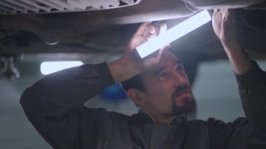 Arabayı aşağıdan inceleyen tamircinin portresi asansörde yükseliyor ve tabanı denetliyor.