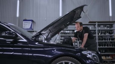 Araba kontrolü ve araba servisinde onarım. Sihirbaz sorun çıkarmak için bilgisayarla birlikte kaputun başında duruyor.