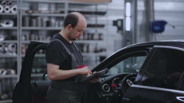 Diagnóstico de coches. Un mecánico en un servicio de primer plano sostiene una tableta en sus manos y presiona la pantalla cerca del coche — Vídeos de Stock