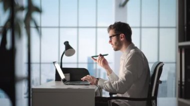 Genç adam cep telefonuyla konuşuyor, not alıyor, ses asistanı kullanıyor, not defteri yazıyor. İçişleri Bakanlığı 'nda dizüstü bilgisayarla oturmuş kulaklık takan gülümseyen adam.