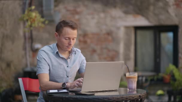 Ανεξάρτητος επιχειρηματίας με γυαλιά που εργάζεται επιμελώς σε φορητό υπολογιστή στο καφέ. Πληκτρολογεί στο πληκτρολόγιο και αναζητά νέα δουλειά στο διαδίκτυο στην καφετέρια — Αρχείο Βίντεο
