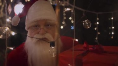 Noel Baba kameraya bakar pencereden bakar ve Noel ışıklarını görür. Noel Baba hediye getirmiş.