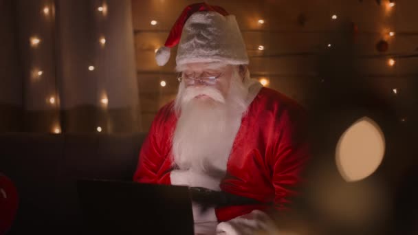 Mikołaj pracuje w domu z laptopem w Wigilię. Światła i dekoracje świąteczne — Wideo stockowe