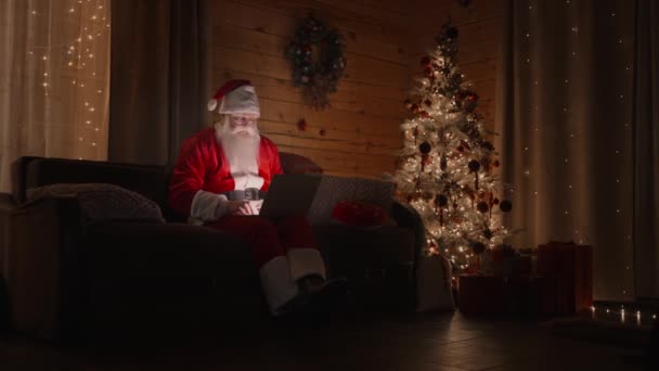 Санта-Клаус работает на ноутбуке отправляет письма с пожеланиями или поздравления по электронной почте на Рождество или Новый год. Санта общается в социальных сетях с детьми по всему миру. — стоковое видео
