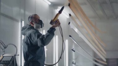 Solunum cihazındaki bir adam metali toz metoduyla boyuyor. Boya dükkanı. Ressam sprey tabanca boyasıyla çalışıyor.